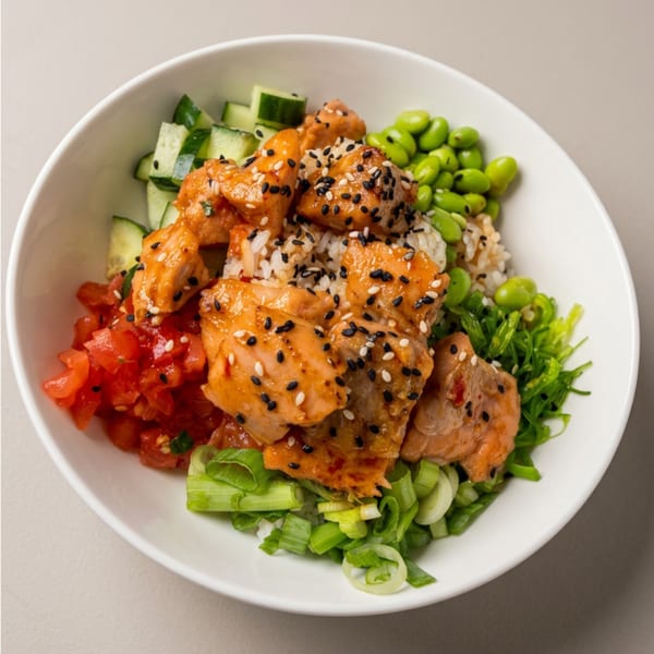 A white bowl filled with salmon poke, rice, edamame, diced tomatoes, cucumbers, and green onions.