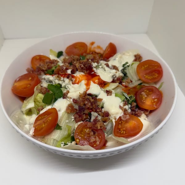 A white bowl filled with a fresh salad, topped with cherry tomatoes, bacon bits, and creamy dressing.